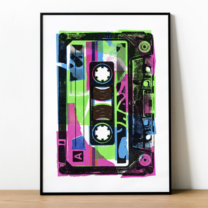 Plakat z kasetą magnetofonową w czarnej aluminiowej ramce stojący na półce